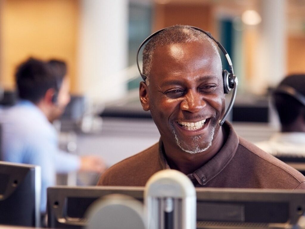 older man in headset smiling in front of computer