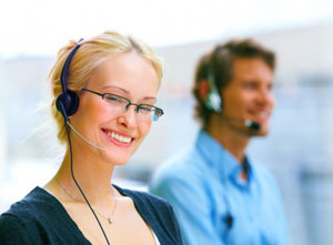female call center agent smiling with headset, another agent sits behind her