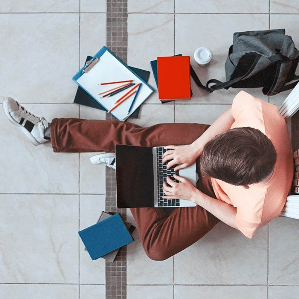 top down view of student on laptop sitting next to pens, paper, and a book bag
