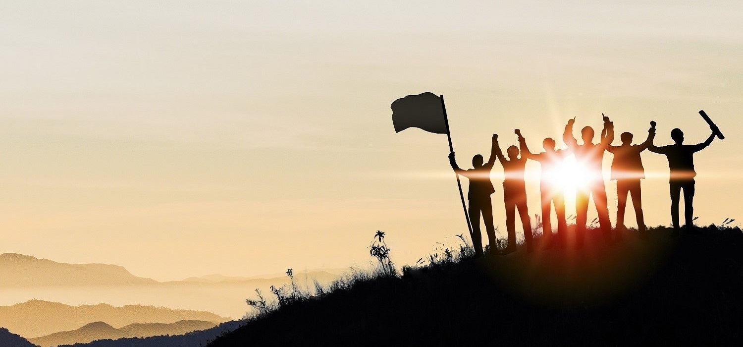 group of people with flag on a hill at sunset