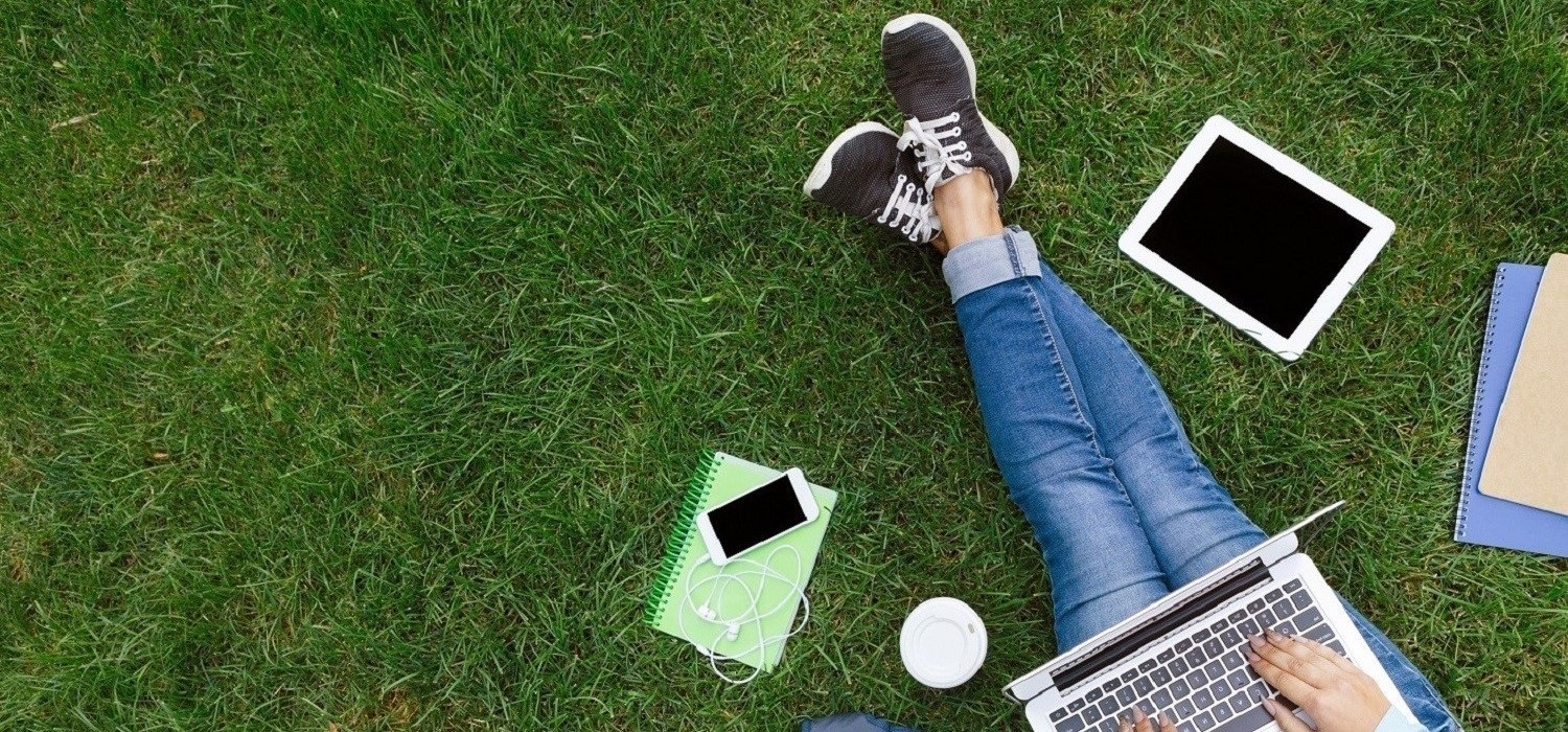 college student laying on grass with laptop, pad, and folders Enrollment Management