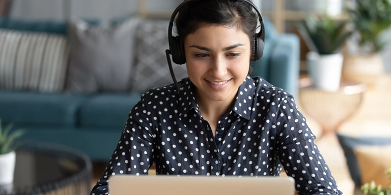 woman wearing headset and polka dot shirt talking to a customer and looking at a computer screen