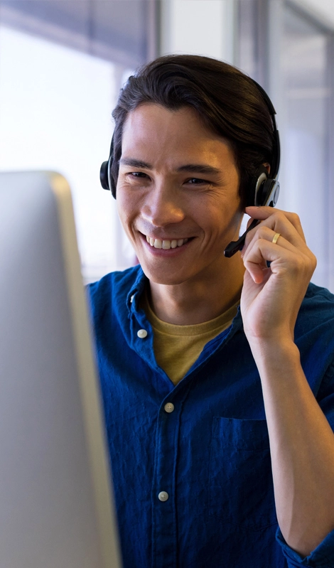 Un amable agente de atención al cliente masculino con auriculares, sonriente mientras ayuda a un cliente en su computadora — representa los servicios de atención al cliente multilingüe de AnswerNet