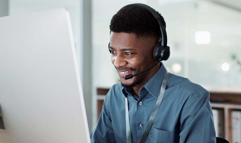 Un agente telefónico masculino con una camisa azul y unos auriculares, mirando un monitor de computadora.