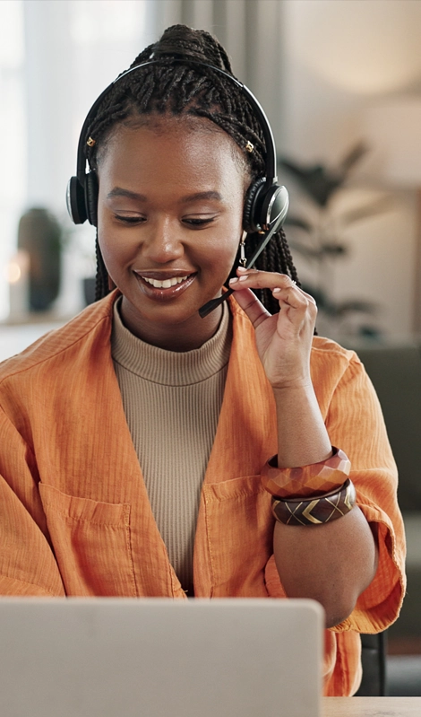 female in a headset wearing an orange jacket looking at a laptop screen