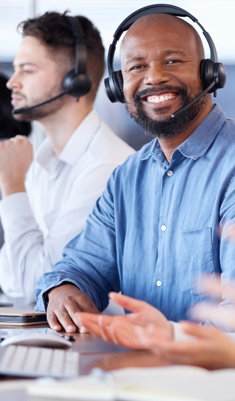 man in blue shirt wearing headset and smiling with another man in a headset behind him